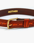 The Eye Opener by Mother is a vintage cow leather belt with decorative patterns and a gold buckle, featuring "MOTHER" printed in gold on the inner side.