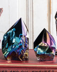The Aura Black Obsidian Points by Blue Ocean Traders feature iridescent crystal points with metallic blue, purple, and gold hues, displayed on a red book among vintage books—a captivating sculptural accent for any space.