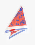 The Clare V Bandana by Clare Vivier is a 20 x 20-inch cotton scarf in red, blue, and white with French text like a concert ticket, striped edges, and a "CLARE V." label sewn in one corner. Photographed on a plain white background.
