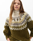 A woman with long, wavy brown hair wears the Rag & Bone beth oversized fair isle tneck sweater with a white, gray, and yellow patterned yoke, standing confidently against a plain white background.