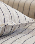 Close-up of beige Blake Big Pillow 28x36 by POM POM, featuring black vertical stripes that accentuate the hand-loomed texture and woven pattern. Part of the same style, another similarly textured surface is interwoven in the background.
