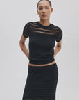 A woman poses against a light background in the Rag & Bone britt ss crew, an airy striped summer sweater with sheer details at the shoulders and sleeves, paired with a matching black textured skirt.
