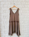 Sleeveless brown slip dress with lace trim by Xirena, cupro viscose fabric, displayed on a hanger against white brick.