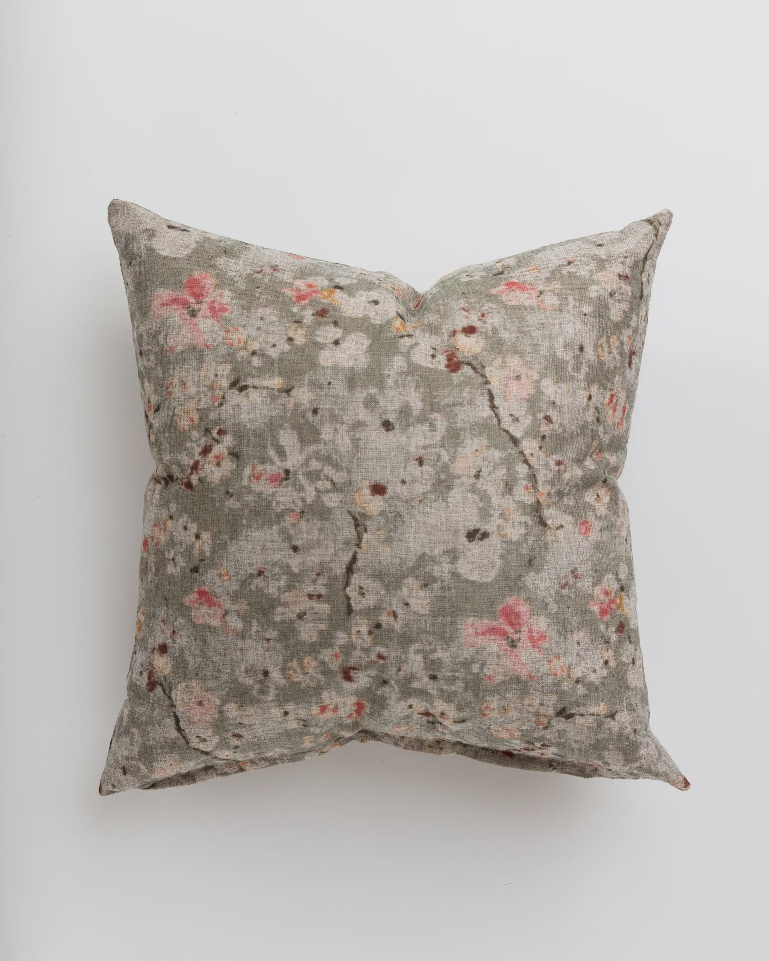 A Gabby Cherry Blossom Taupe Pillow in 26x26 inches with a floral pattern in muted pink and orange hues on a gray background, photographed against a white surface in a Scottsdale, Arizona bungalow.