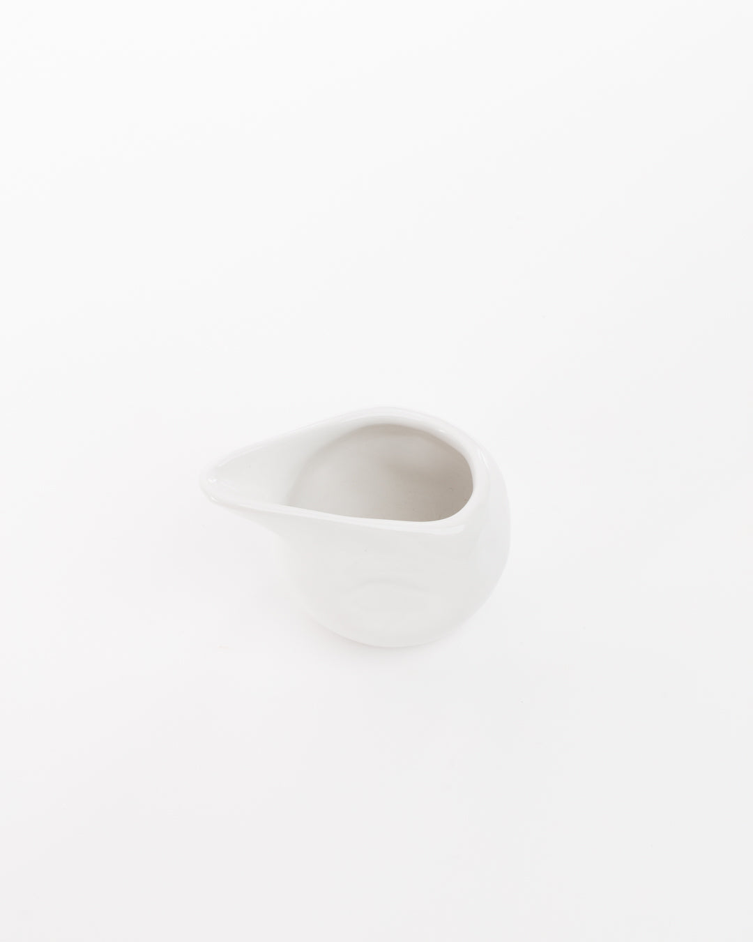A small, white ceramic pitcher with a round body and a narrow spout, crafted using traditional techniques, set against a plain white background. The handmade ceramic dinnerware piece - the Gravy Boat 374 by Montes Doggett - is viewed from above, slightly tilted, showing the opening and inner part.