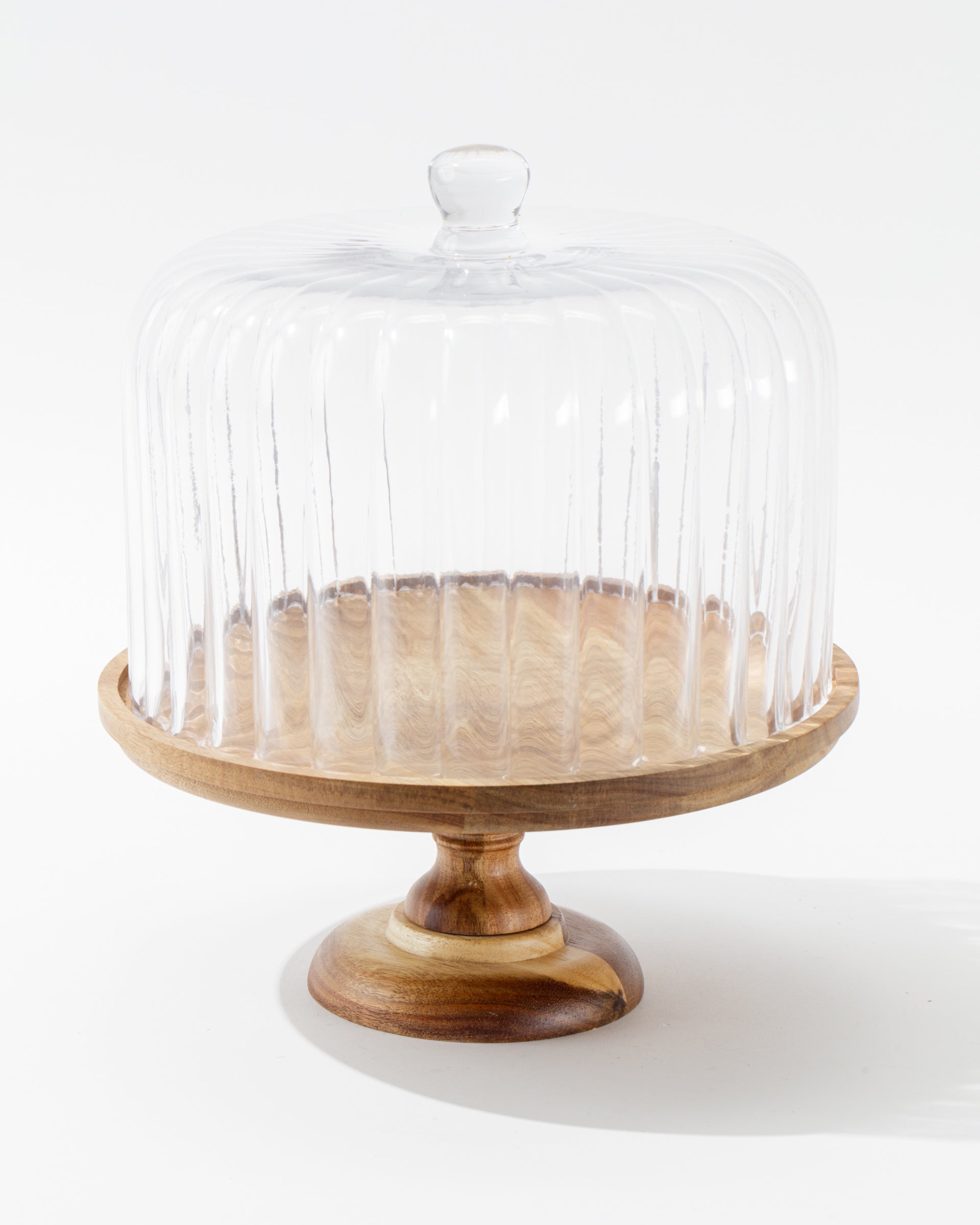 The Creative Co-op Cake Cloche features a wooden pedestal with a round base and a clear ribbed glass dome, shown against a plain white background.