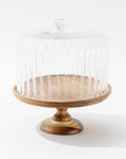 The Creative Co-op Cake Cloche features a wooden pedestal with a round base and a clear ribbed glass dome, shown against a plain white background.
