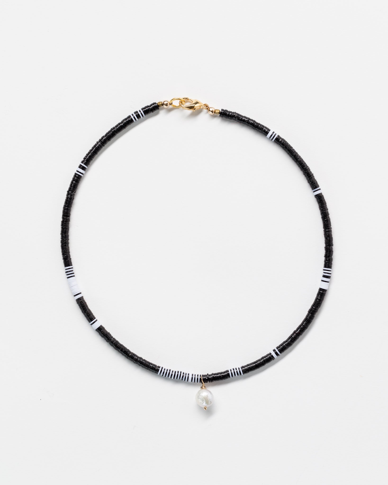 A Designs By Raya necklace with black and white beads and a single pearl, styled with gold clasps, displayed on a plain white background.