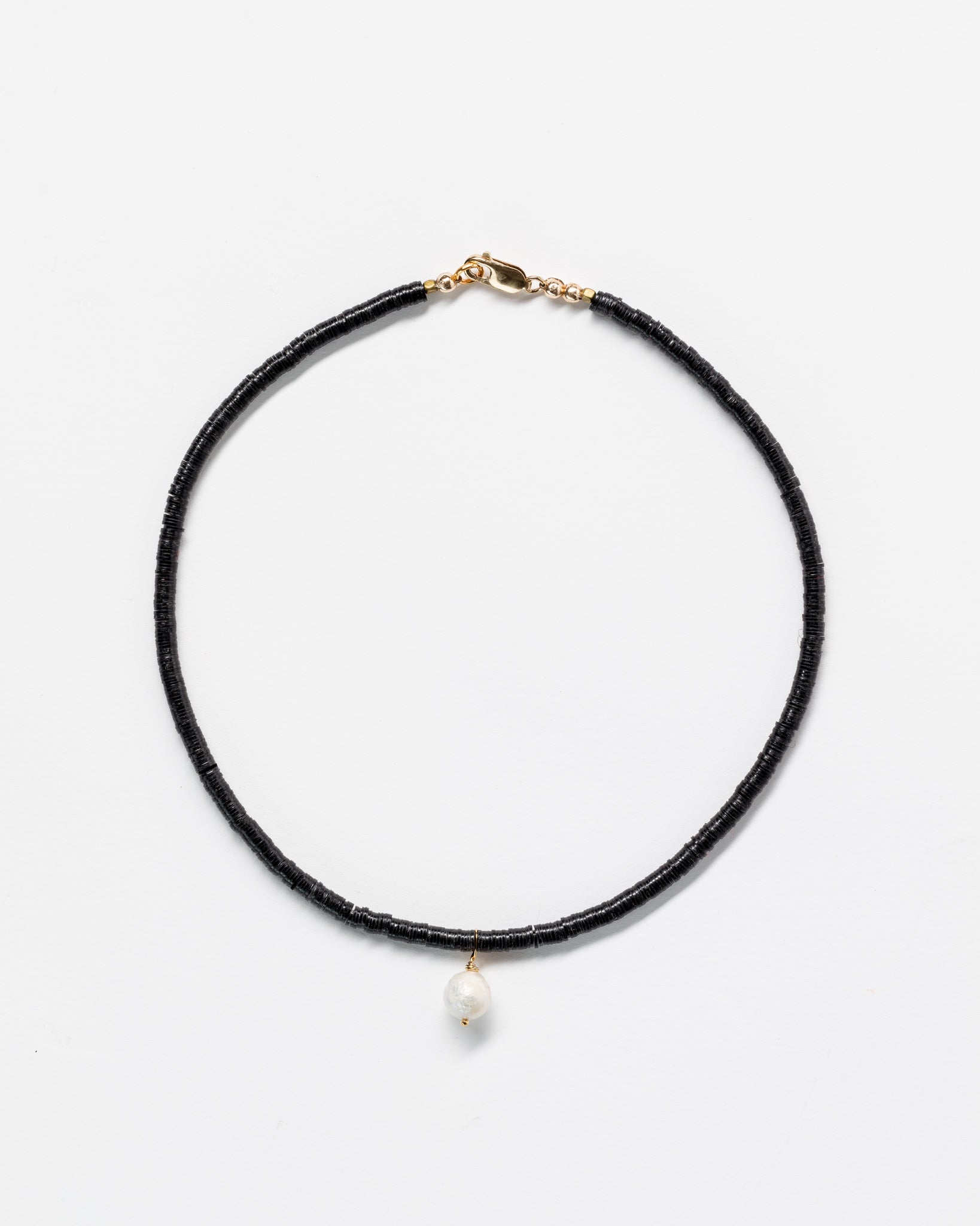 A simple black Designs By Raya choker necklace with a single pearl pendant and a gold clasp, displayed against a plain white background in Arizona style.