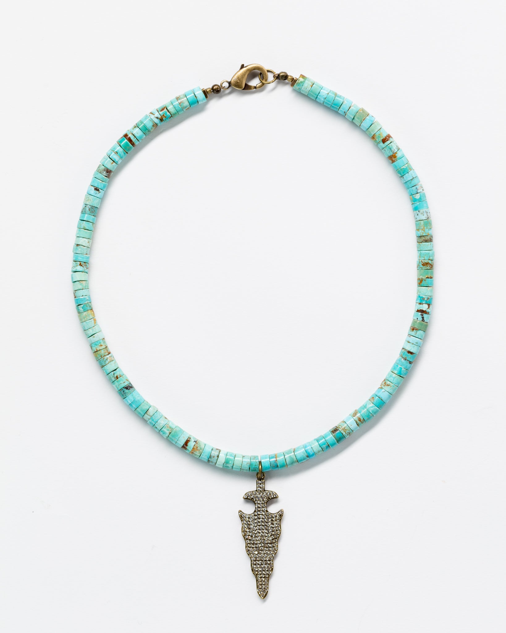 A Designs By Raya necklace with turquoise and gold beads in an Arizona style and a detailed gold pendant shaped like an arrowhead, displayed against a plain white background.