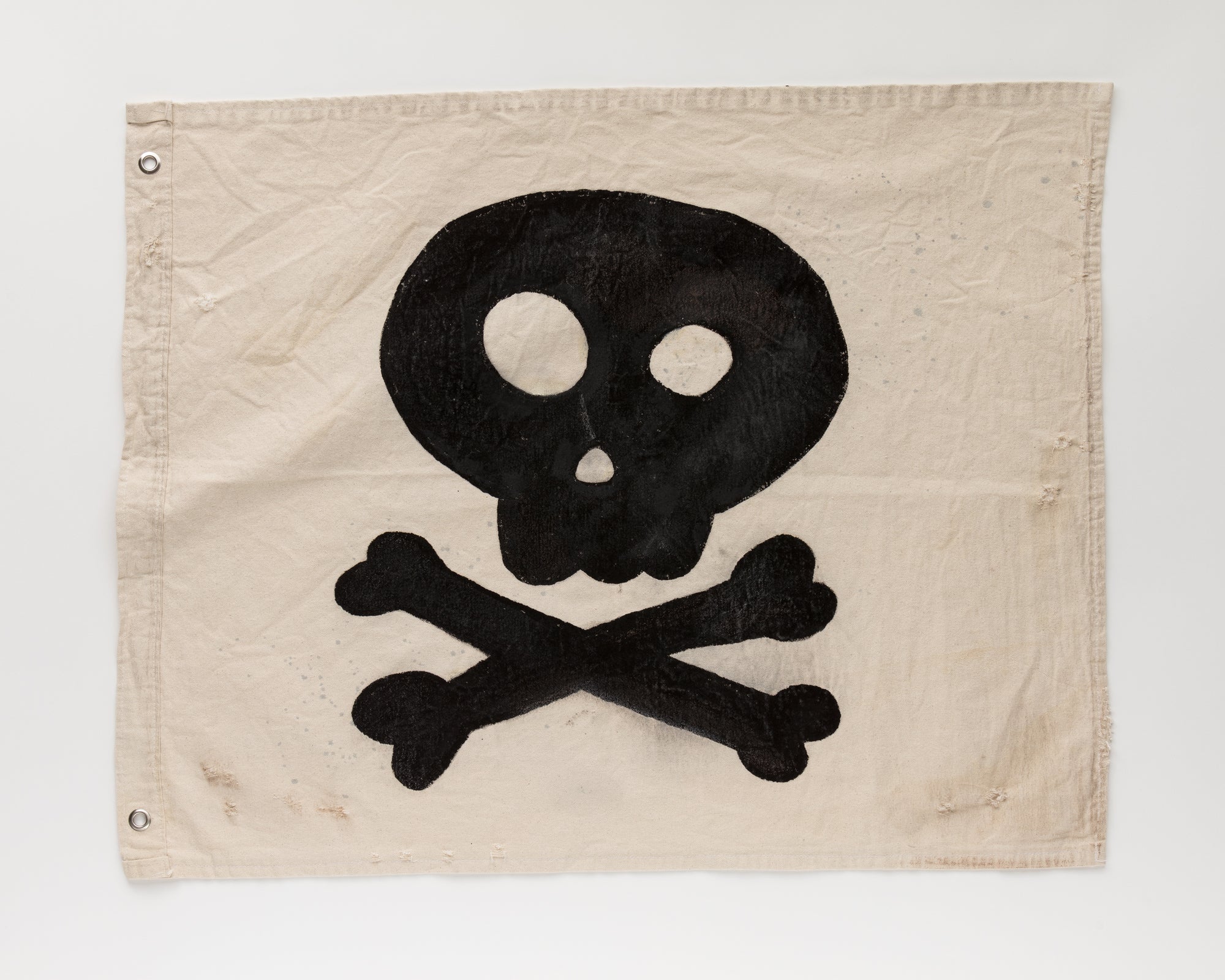 The Camp Flags 26x33 from Tak Design features a distressed beige canvas showcasing a black skull and crossbones design in the center, exuding vintage Halloween charm. The skull's large, round eye sockets and small, round nose add character, while metal grommets in the corners enhance its rustic aesthetic.