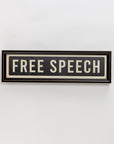 The "Street Sign In Black" by Spicher And Company is a rectangular sign with a black frame and white background reading "FREE SPEECH" in bold black letters—an eye-catching piece of wall decor for any space.