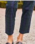 A person stands on gravel wearing Frank & Eileen's WICKLOW The Italian Chino in Italian Performance Twill featuring four-way stretch, paired with black loafers. Blurred greenery forms the background.