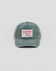 The CLOSED Cap is a green cotton hat with a washed finish, featuring a rectangular white patch on the front with red "CLOSED PRODUTTORE DI JEANS DAL 1978" text, an adjustable strap, and shown against a plain light background.
