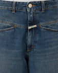 Close-up of a person wearing CLOSED Baggy Shorts crafted from recycled cotton denim, featuring a distinctive overlapping waistband with a silver button and metal brand tag, paired with a white top.