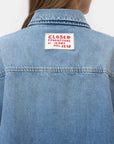 A person seen from the back wears the CLOSED Oversized Shirt in light blue denim, featuring a white patch near the collar with "CLOSED PRODUTTORE DI JEANS DAL 1978" in red—an understated Italian-inspired detail.