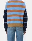 A person wearing blue jeans and the CLOSED Crewneck LS Knit—an alpaca wool sweater with blue, orange, and beige horizontal back stripes, plus navy sleeves with lighter blue stripes—stands against a plain white background.