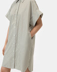Someone wears the CLOSED Turn-up Shirtdress, a loose-fitting, short-sleeved cotton shirt dress with green and white vertical stripes and mother-of-pearl buttons, posing with one hand in their pocket against a plain white background.