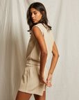 A woman with medium-length dark hair models the Perfectwhitetee Carli Muscle Tank and matching shorts in a relaxed fit, standing sideways against a light, textured backdrop and looking over her shoulder at the camera.