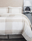 A neatly made bed with the Amity Home Chalmers Quilt Nat K and matching pillows sits beside a small table holding a black lamp, a clock, a “Tom Ford” book, and a candle.