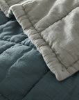 A close-up of the Amity Home Spencer Quilt shows reversible blue slub cotton on one side and light gray on the other, highlighted by visible stitched seams.