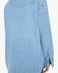 The image displays "The Exes And The Ohs" by Mother, a light blue denim shirt in vintage-blue wash with long sleeves, a Western-style yoke at the shoulder, and buttoned cuffs. It has a textured look and is paired with blue jeans.