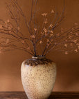 The Large Rustic Ceramic Urn by Kalalou, Inc features a mottled beige and brown finish and holds bare branches with dried buds, set on a wooden surface—an ideal striking entryway accent.
