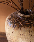 A close-up of the Kalalou, Inc Large Rustic Ceramic Urn with a brown and cream glaze, filled with thin branches and dried berries—ideal for adding charm to your entryway decor.