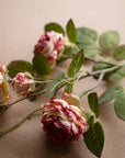 A close-up of three pink and cream Kalalou, Inc Garden Rose artificial flower stems with green leaves on a beige surface—ideal for spring arrangements.