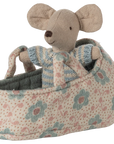 The Maileg Baby Mouse in Carry Cot by Maileg features a baby mouse in a striped sweater nestled inside a soft, floral carry cot with two handles.