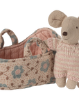 The Maileg Baby Mouse in Carry Cot by Maileg features a tiny mouse dressed in a pink knitted suit, standing next to a floral carry cot basket with handles.