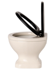 Side view of the Maileg Water Closet by Maileg, featuring a white toilet with a black seat and upright lid, perfect for small spaces or as a mouse toilet. Set against a light background, it suits any SuitCasa bathroom decor.