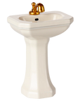The Maileg Furniture by Maileg features a cute small white pedestal sink with a gold faucet and black drain, perfect for dollhouse or Maileg Mouse setups, shown on a plain white background.
