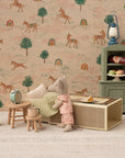 The Maileg Little Sister Mouse / Matchbox by Maileg wears pajamas and stands in a cozy scene with a bed, nightstand, clock, and stool. A backdrop with horses, trees, and rainbows adds a whimsical touch to this charming collectible.