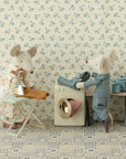 Two Maileg mice from the mouse family bustle in a dollhouse laundry room, using the Maileg Washing Machine. One mouse irons clothes while another loads laundry, with cozy accessories like a wardrobe and table set against floral wallpaper.