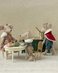 Three Maileg mice in royal outfits gather for tea at a tiny table with cups and pastries. One stirs a pot on a green stove, while the Maileg Gold Chair by Maileg adds charm to this whimsical, cozy tea party scene.