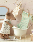 A brown fabric mouse in a dress washes clothes beside the Maileg Bathtub. Clothes hang above, with a sink, mirror, and stool with clothespins adding charm to this dollhouse scene featuring Maileg accessories.