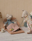 Two Maileg stuffed mice relax in a cozy living room: one naps under a blanket on a polka-dot bed while the other, in an apron, vacuums by the Maileg Sofa Bed. A lamp, teacup, and teapot complete this inviting Maileg brand scene.