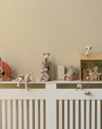 A white shelf displays Maileg toys—including the Maileg Pumpkin Carriage, royal mice, and miniature furniture—set in whimsical, fairytale-inspired scenes against a beige wall for a playful decorative touch.