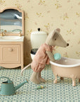 The Maileg Big Sister Mouse, Matchbox, wears pink pajamas and stands by a pink bathtub with sponge, sink and mirror, toilet, green watering can, bottle, and patterned floor—ideal to pair with soft bedding or matchbox toy accessories.