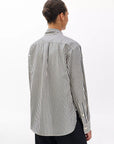 A person with dark hair in a bun is seen from behind wearing the Rag & Bone connie striped shirt—black and white vertical stripes—paired with black pants, set against a plain white background.