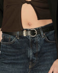 Wearing Janessa Leone’s Myra top—a brown, cropped cut-out style—with dark blue jeans and a black belt, one hand in pocket. The midriff and part of the torso are visible.