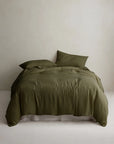 Olive green linen duvet cover by Cultiver Goods on a neatly made bed with two pillows against a light wall.