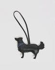 The Clare Vivier Coqui Fob is a black dog-shaped smooth leather keychain with a looped strap and blue collar, perfect as a playful accessory, shown on a plain white background.