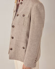A person wearing the Maison Hotel Nehru Jacket in beige with large brown buttons, patch pockets, a printed scarf, and cream dotted pants, styled with Indian tailoring details and shown from the side against a neutral background.