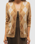 A woman models the Brazeau Tricot Argyle Cardigan in tan and brown with a button-down front, layered over a brown dress, shown from shoulders to hips against a plain background.