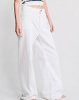 A person models Denimist’s DECK PANT WHITE WASH in white denim, paired with a striped short-sleeve top and white sandals, standing against a plain light background. The image is cropped below the shoulders.