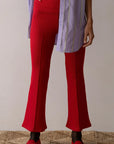 A person is wearing a lavender and white striped shirt, Donni's The Rib Kick Flare red pants, and matching red shoes. They are standing on a textured beige rug, captured from the neck down.