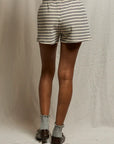 A person stands facing away, wearing Perfectwhitetee French Terry Shorts with an elastic waistband, gray socks, and brown shoes against a light-colored fabric backdrop.