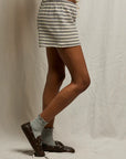 A person stands sideways in Perfectwhitetee French Terry Shorts with an elastic waistband, paired with gray socks and brown loafers. Only the lower half of their body is visible against a neutral fabric background.